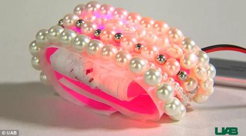 Smart bracelet device, looks like a neon pink bracelet adorned with pearls, wires trail out the back of the device